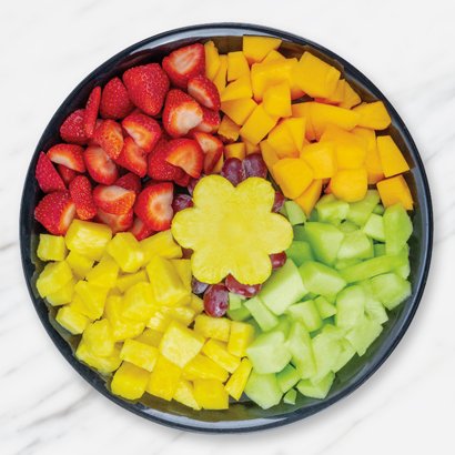 A round tray of colorful sliced fruit in sections, with a flower-shaped pineapple center.