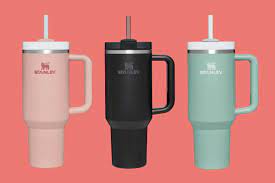 Three Stanley tumblers with handles: pink, black, and mint green on a coral background.