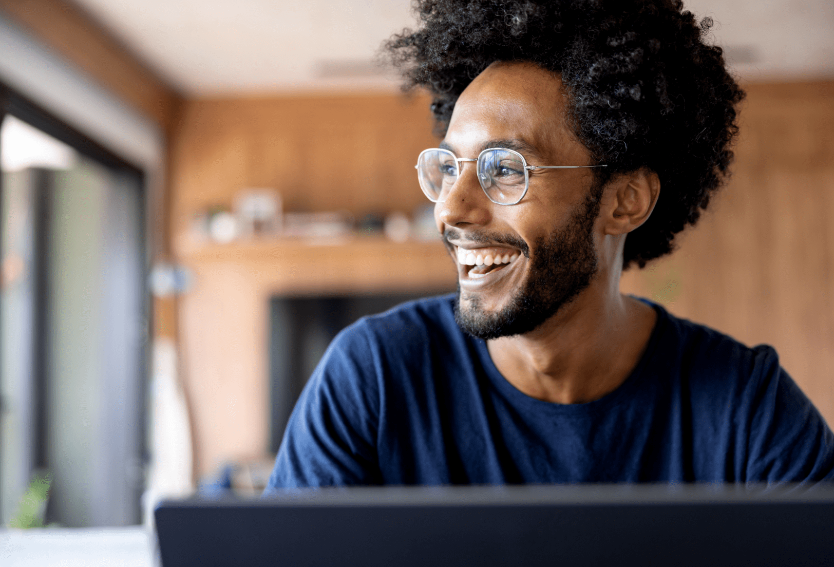 An african american man smiles from behind his laptop